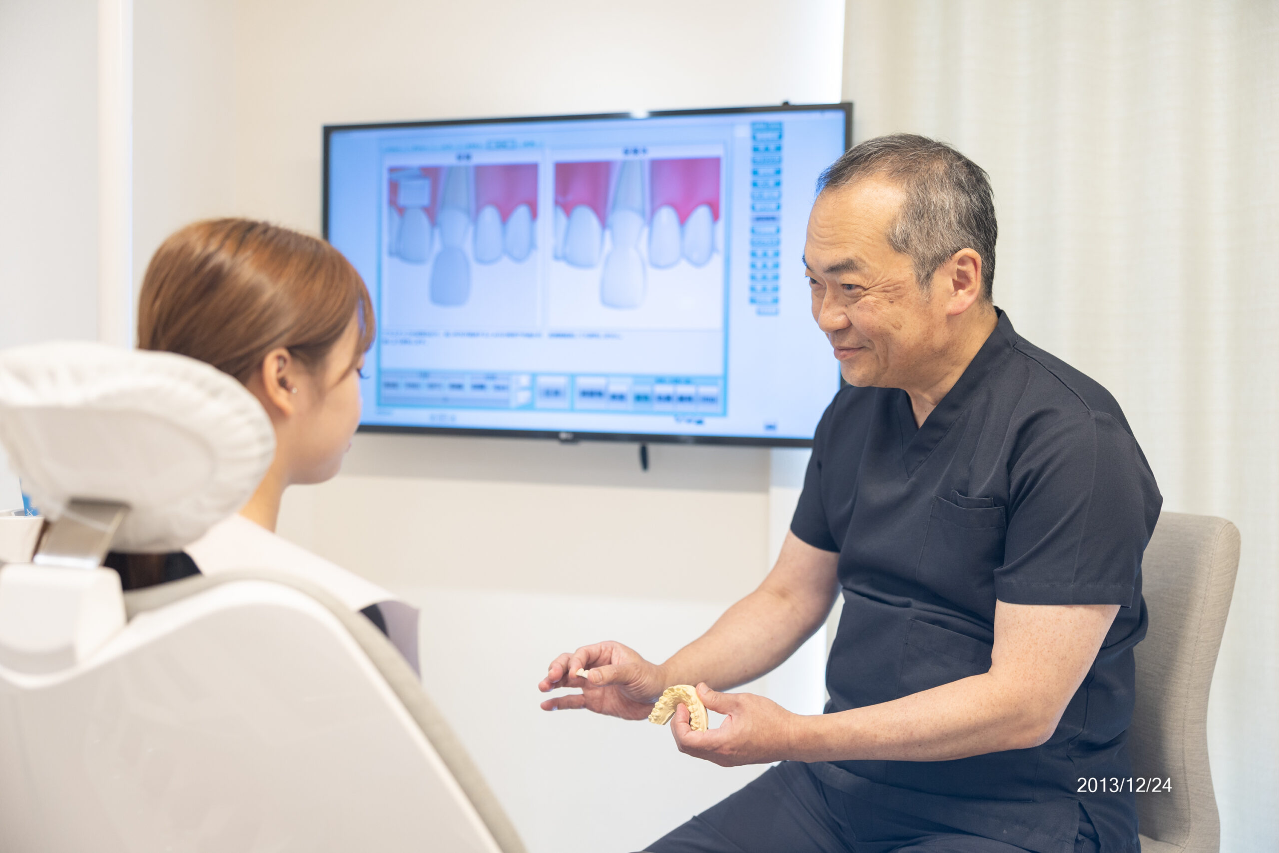 歯の模型を手に、モニターの説明画像を使って患者にカウンセリングする男性歯科医師